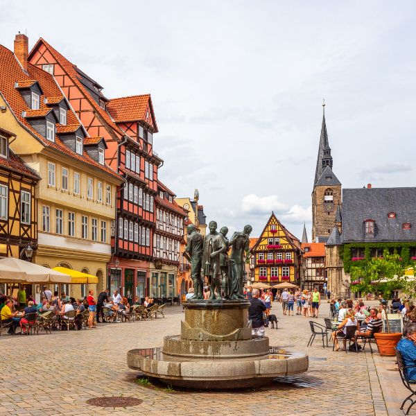 people around a water fountain in square with half-timbered houses and church in  Quedlinburg Square, Germany